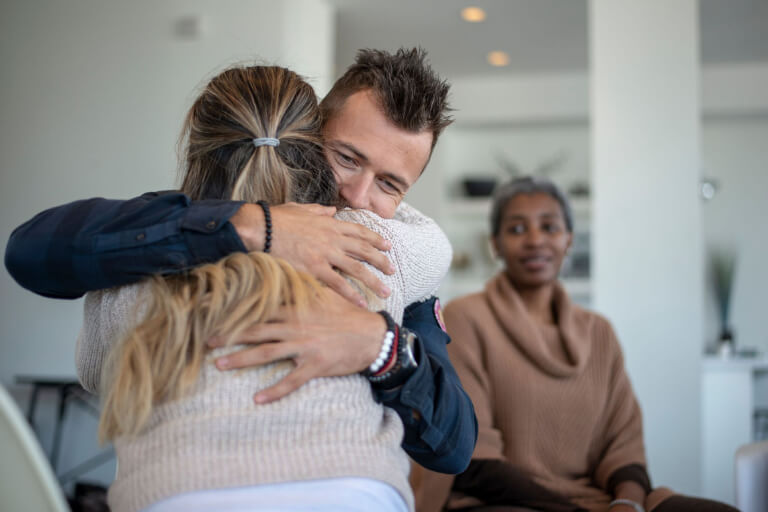 Two people hugging while a third person watches.