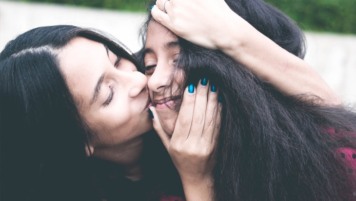 Mother kissing her teenager daughter on the cheeks