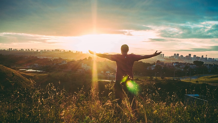 Happy man facing the sunshine with arms outstretched