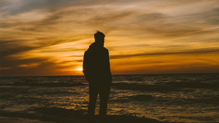 Silhouette of a person standing in front of the beach during sunset