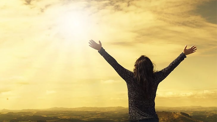 Happy woman facing the cloudy sun