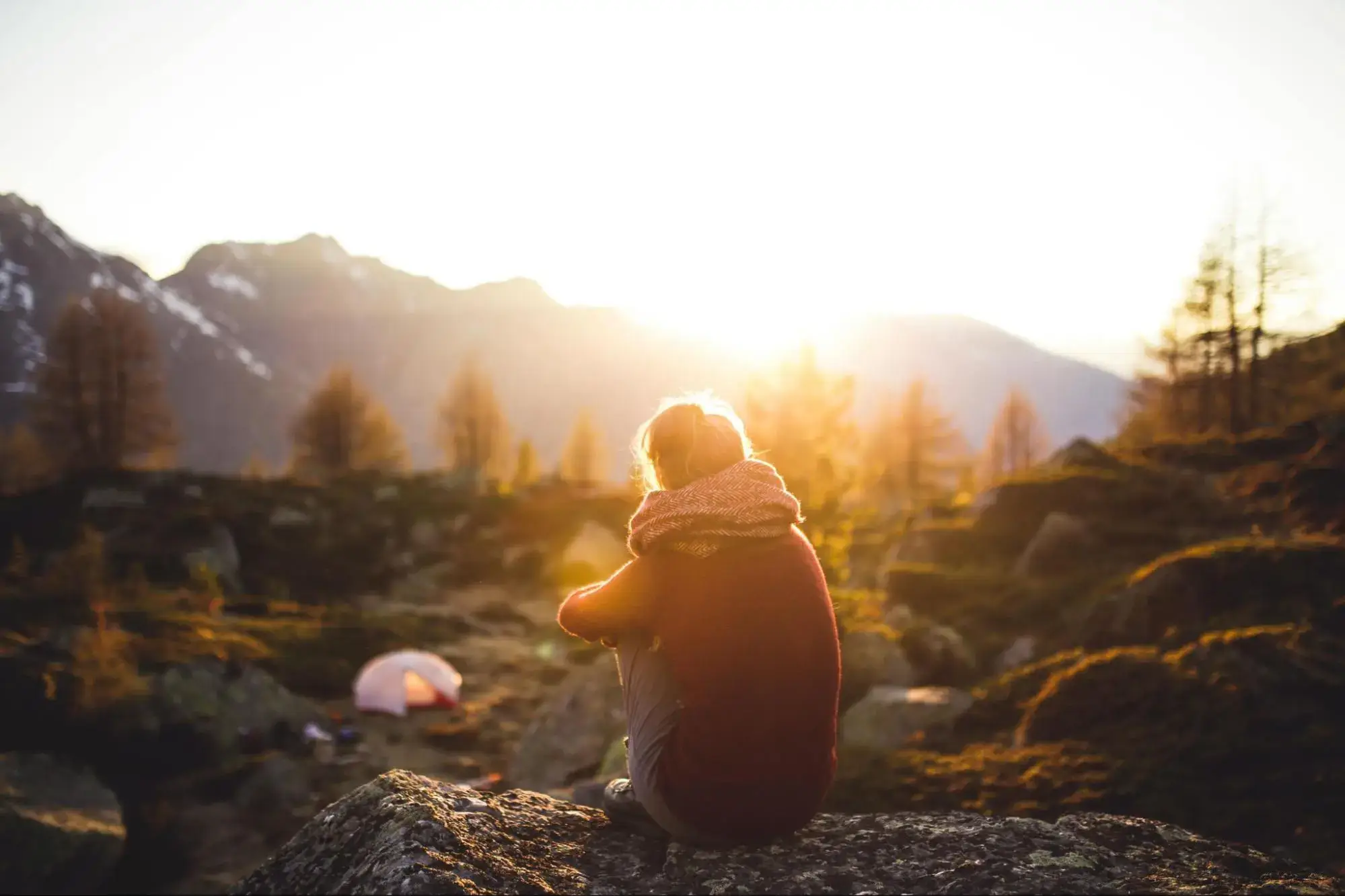 Woman sitting outside on a rock watching the sun set