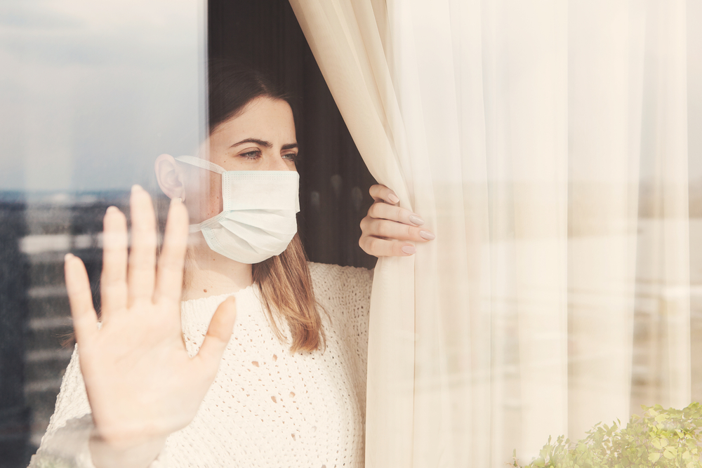 Woman wearing a mask in isolation seen from a glass window.