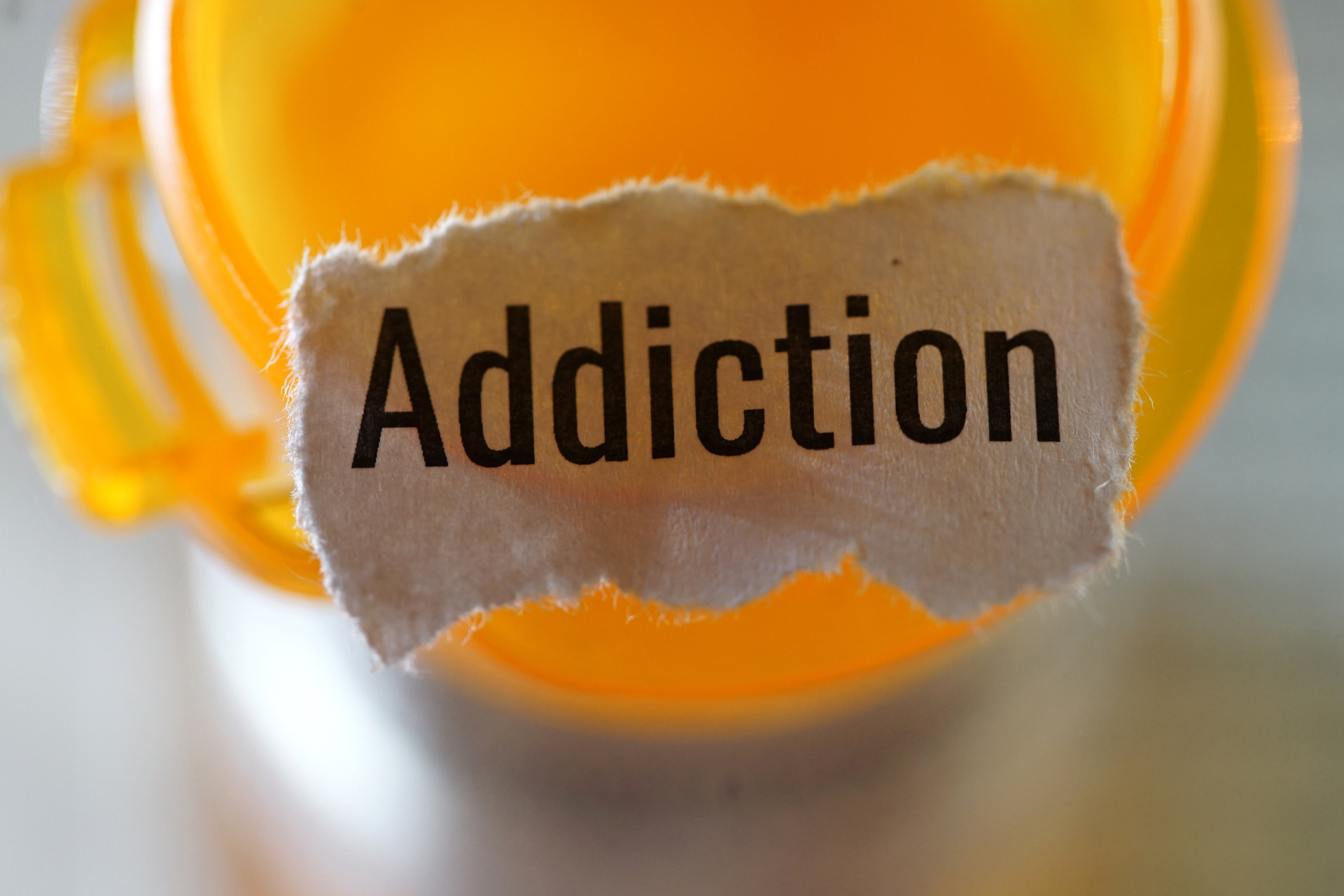 a prescription bottle with a scrap piece of paper that reads “addiction”.