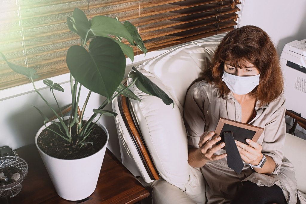 a masked woman looks at a framed picture longingly