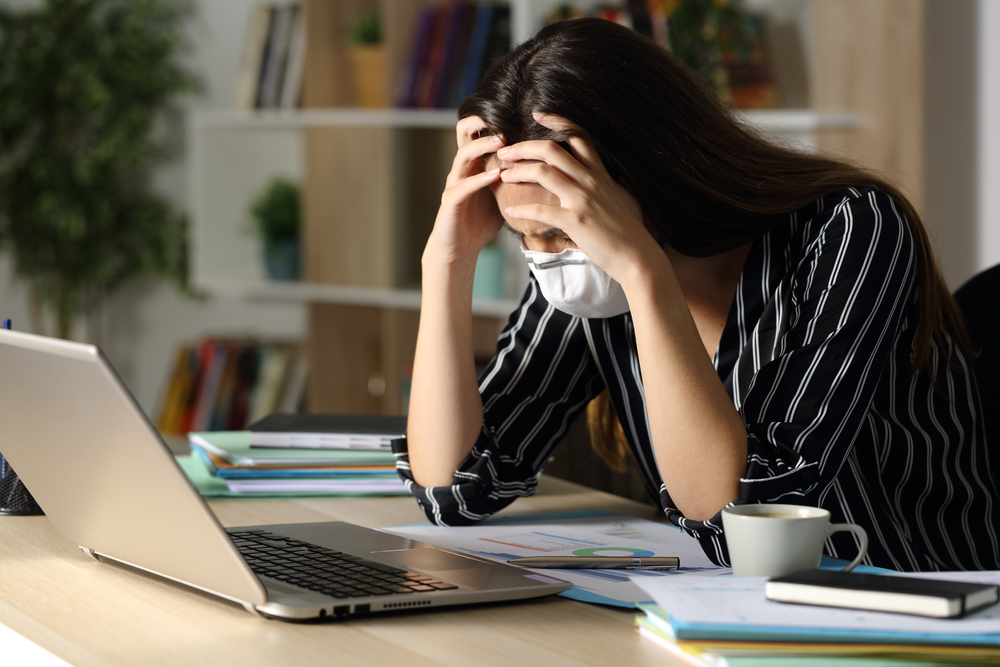 Sad woman wearing a mask in front of her laptop