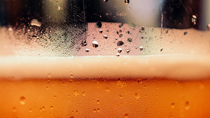 A macro shot of an ice-cold glass of beer with foam on top