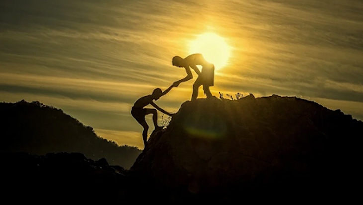 A man lending a hand to help another man get on top of the hill.