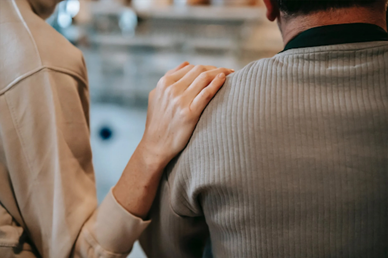 A person comforting someone by patting them on the shoulder