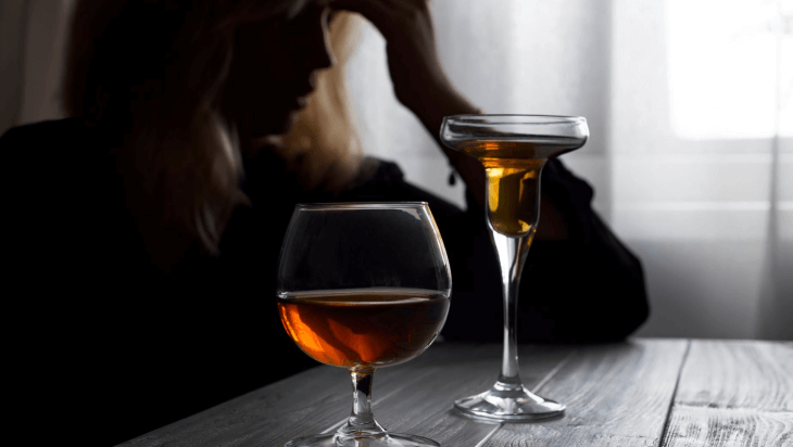 A woman seated next to two alcoholic beverages on a table.