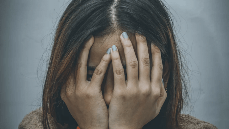 A young woman covering her face with her hands.