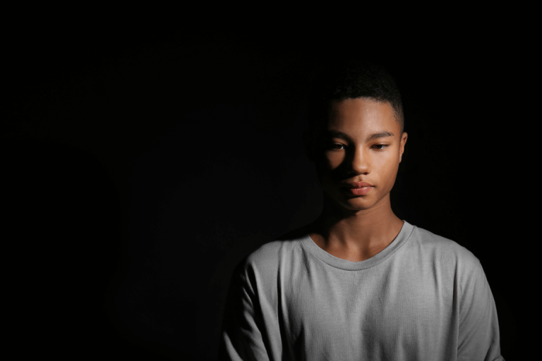 A teenage boy looking sad in front of a black background