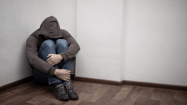 A person curled up in a corner of their room.