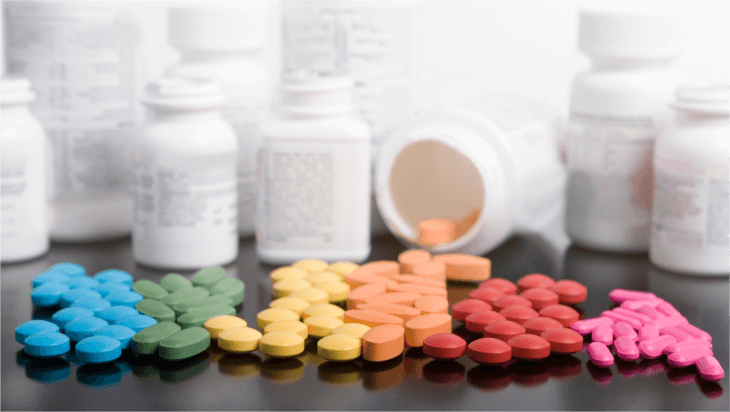 Several pill bottles spill out to reveal rainbow coloured prescription medication