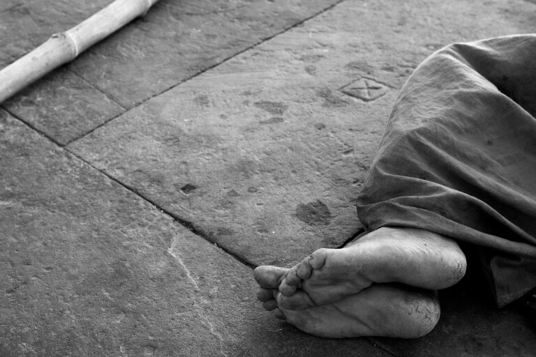 a black and white photo of a person with no shoes on laying on the street
