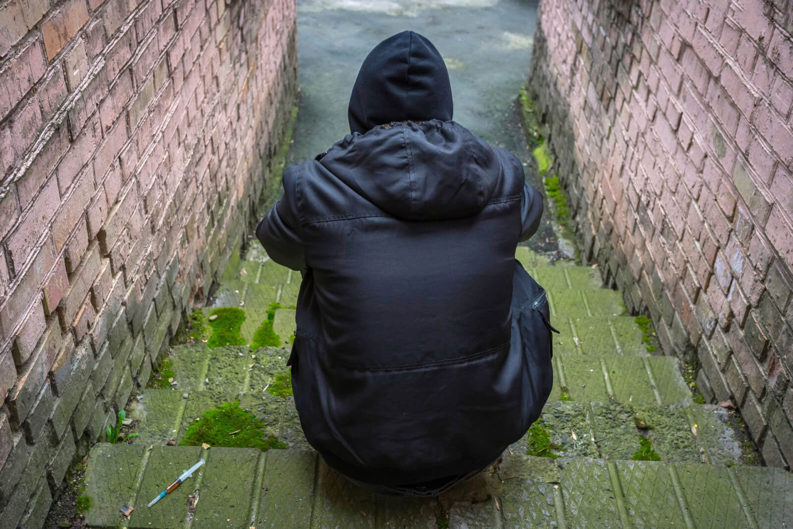 A man sitting on stone steps with a syringe beside him