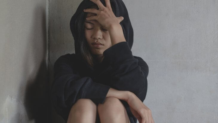 a distressed woman clutching her forehead in the corner of a room