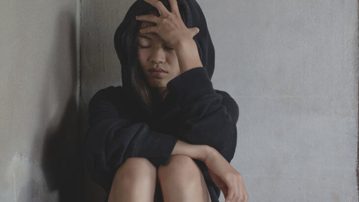 Woman wearing a black hoodie sitting against a wall