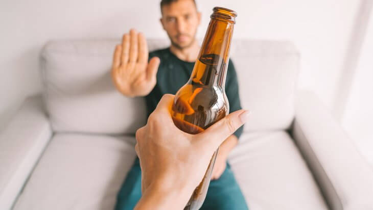 Man sitting down and gesturing no to a bottle of alcohol