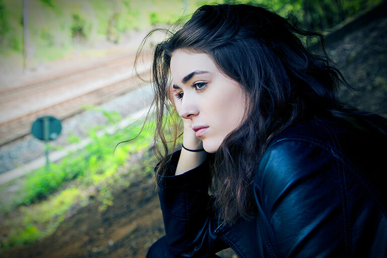 A woman sitting with her head in her hand looking down a train track