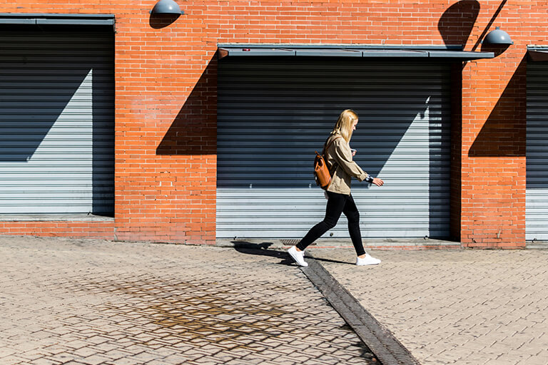 A woman wearing a backpack walks on a cobbled path lined with garage doors