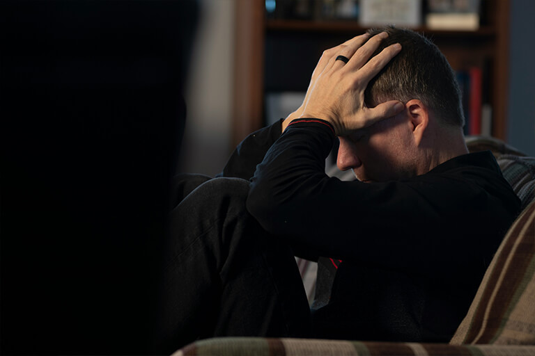 A man wearing a black sweater sits with his head in his hands