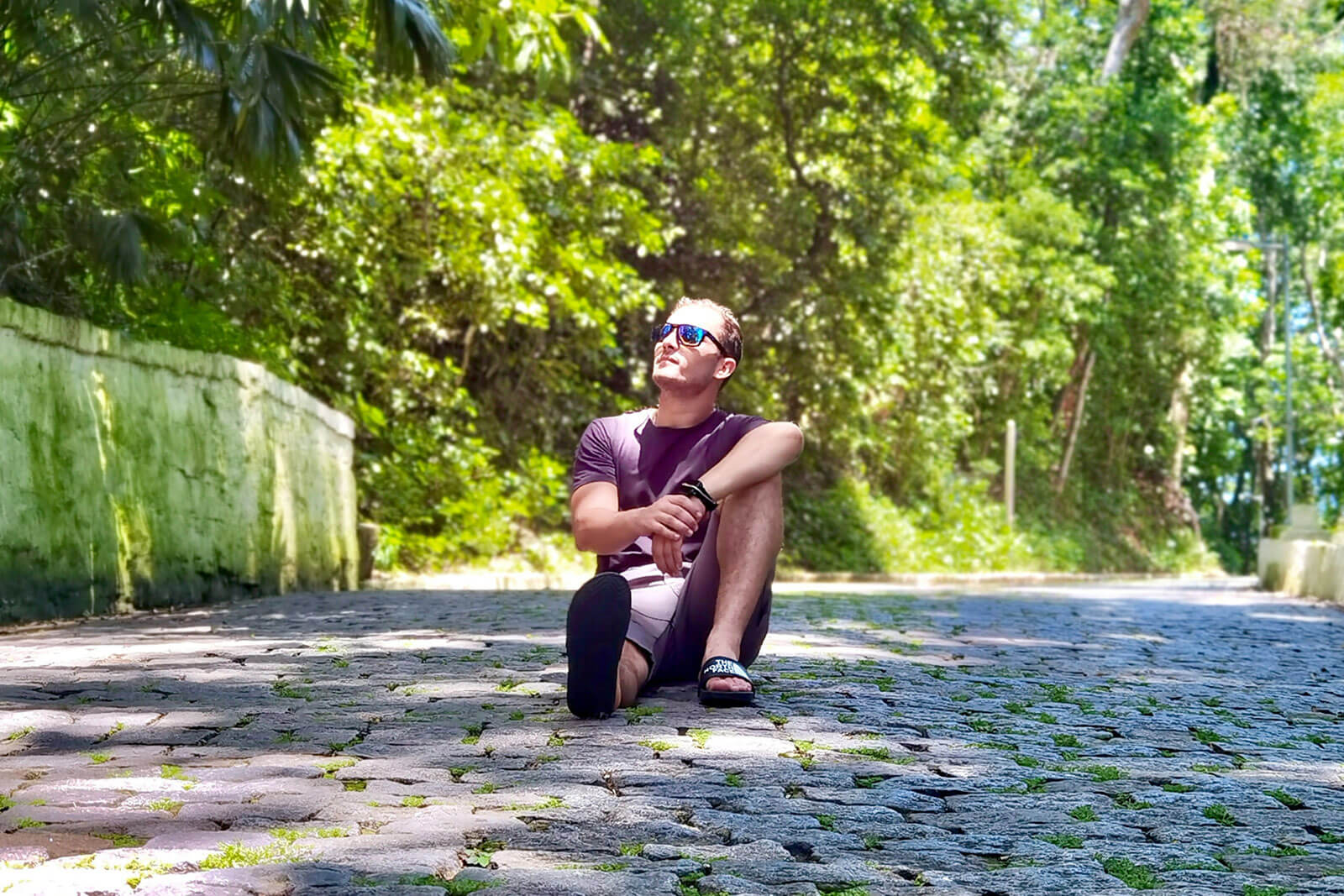A man sitting on a cobblestone path looking up at the trees