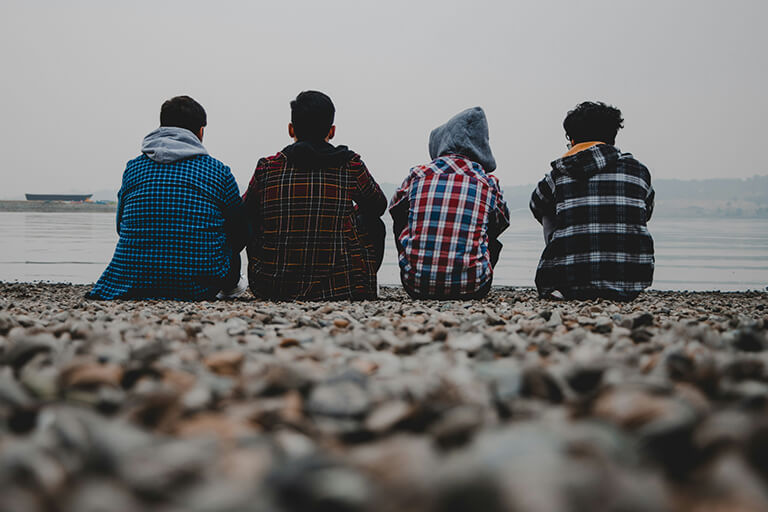 Four teenagers sitting on a rocky beach looking out at the water