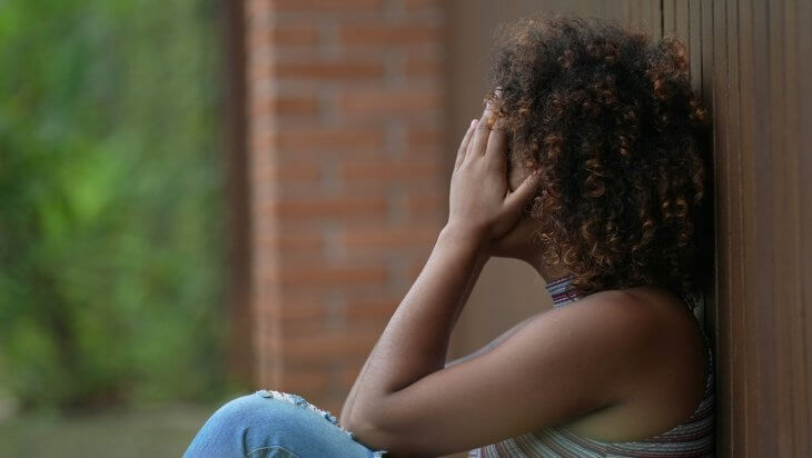 A woman sits against a wall with her head in her hands