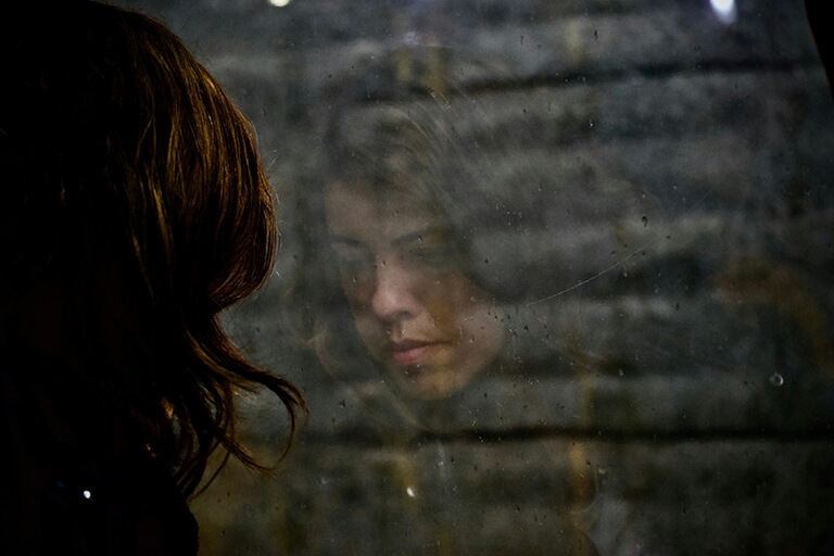 A woman looking out a window with her reflection in the glass