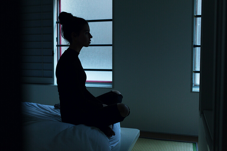 A woman sitting on the edge of her bed in the dark