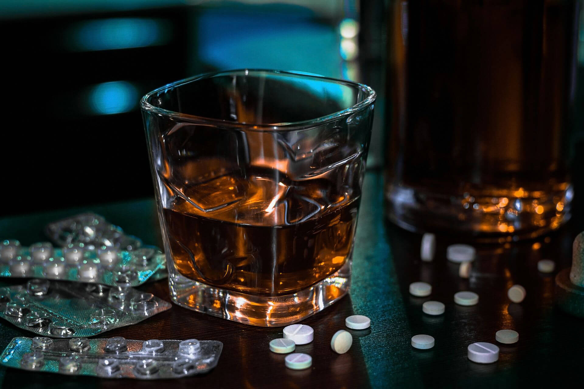 A glass of alcohol with scattered pills on a table