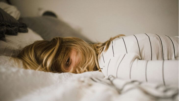 A woman lying face down on a bed with hair over her face