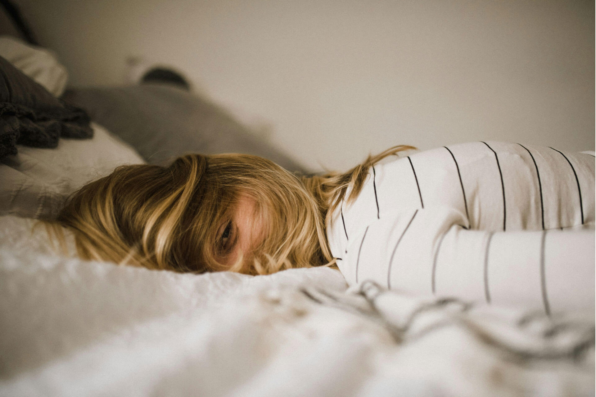 A woman lying face down on a bed with hair over her face