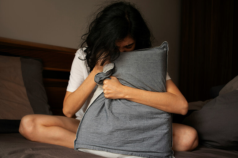 A woman with her head in a pillow as she holds it