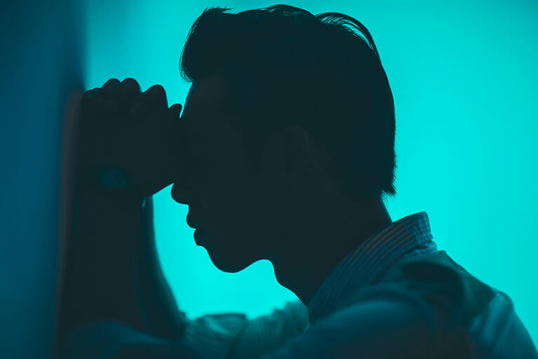 A man leaning his forehead against a wall in a blue-lit room