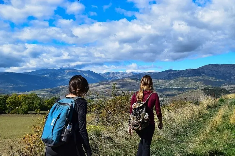 Two women hiking in a field with hills in the background.