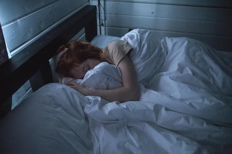 A woman sleeping under a white duvet.