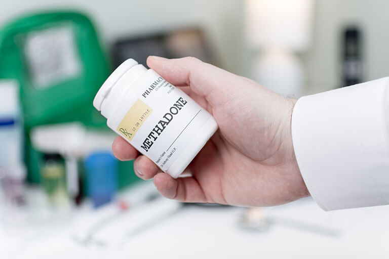 A hand holding a bottle of prescribed methadone