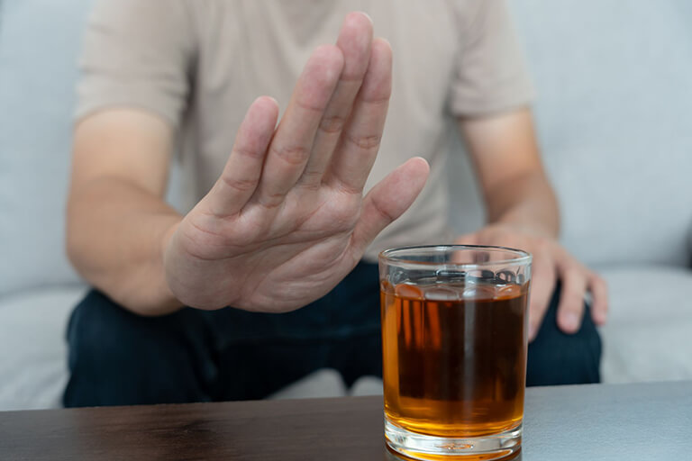 A man sitting down with a hand in front of an alcoholic beverage