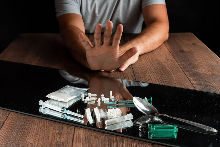 Person saying no to a collection of drugs, from powdered to pills, on top of a mirror