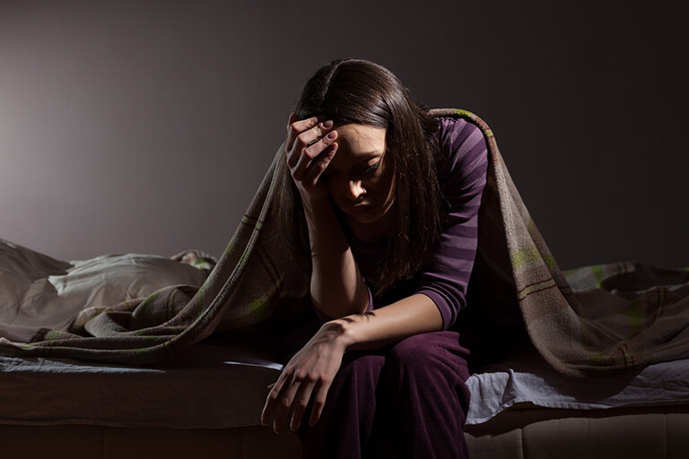 A woman in a dark bedroom holds her head