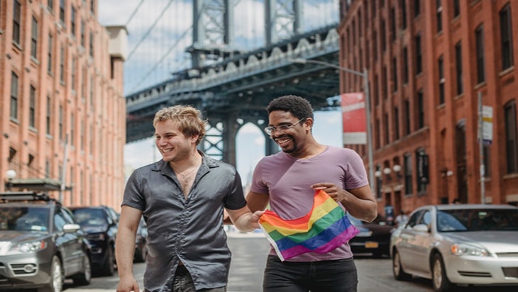 Happy gay couple strolling the street with the Pride flag