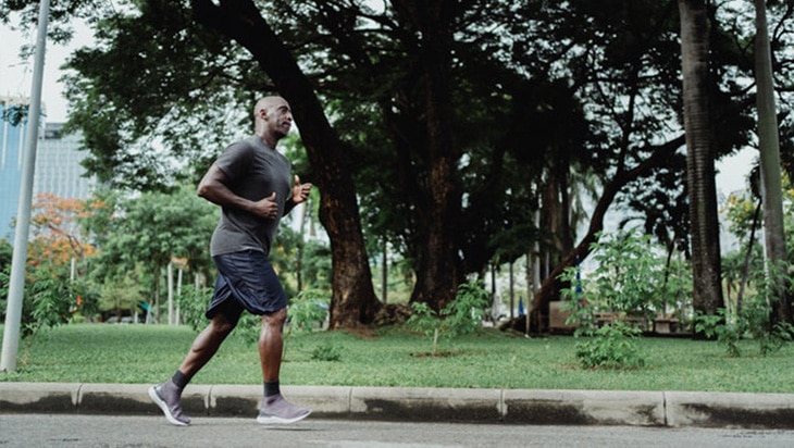 A man in gray shirt and black shorts jogging in a park