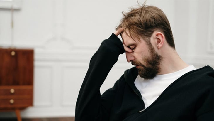 Man in a white shirt and black hoodie looking dishevelled and depressed
