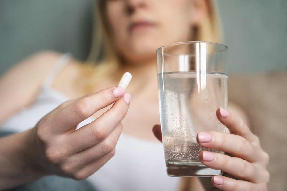 Woman holding a white capsule and a glass of water