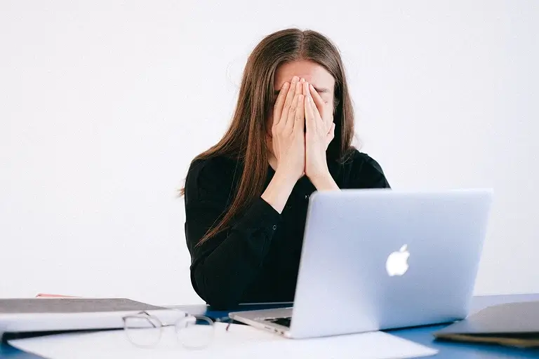 A stressed woman in the office holding her face in her hands
